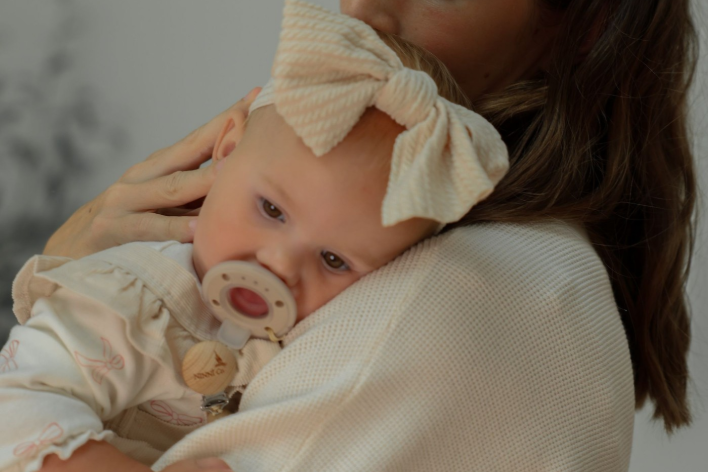 a parent soothes their baby in their arms, who is sucking on a Ninni pacifier